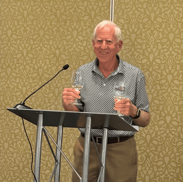 Man smiling, holding two wine glasses.