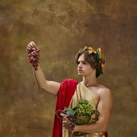 Man in toga holding grapes and fruit.